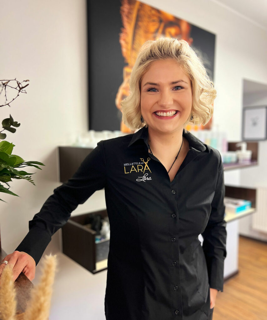 Fröhliche blonde Frau in einem schwarzen Hemd in einem modernen Friseursalon.