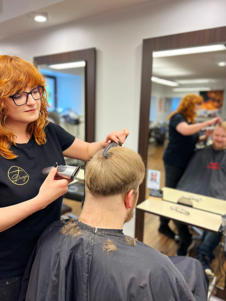 Friseurin mit roten Locken schneidet Haare eines Kunden im modern ausgestatteten Friseursalon.