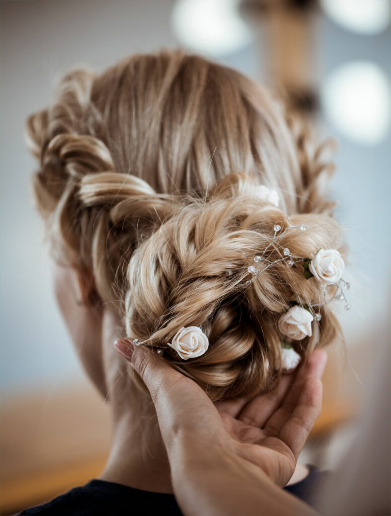 Detailansicht einer eleganten Hochzeitsfrisur mit Zöpfen und weißen Rosen verziert.