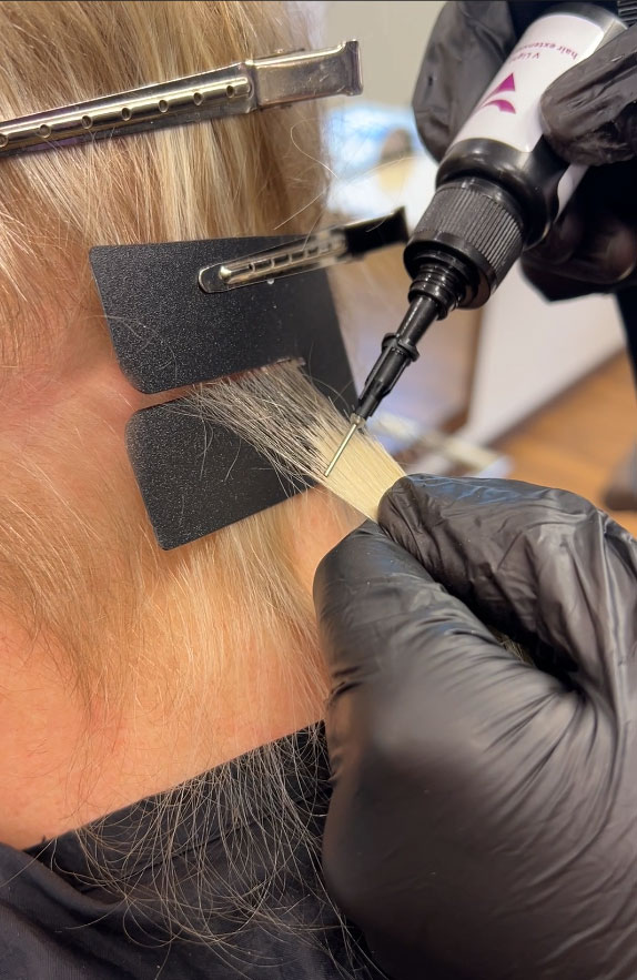 Nahaufnahme des Haarverlängerungsprozesses mit schwarzen Handschuhen und Spezialwerkzeugen.